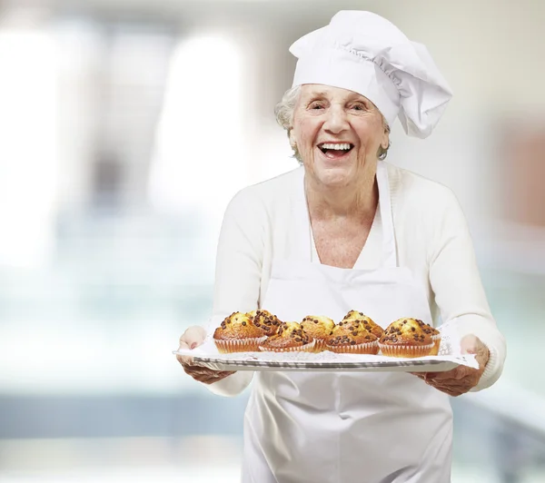 Senior woman cook holding a tray with muffins, indoor — Stock Photo, Image