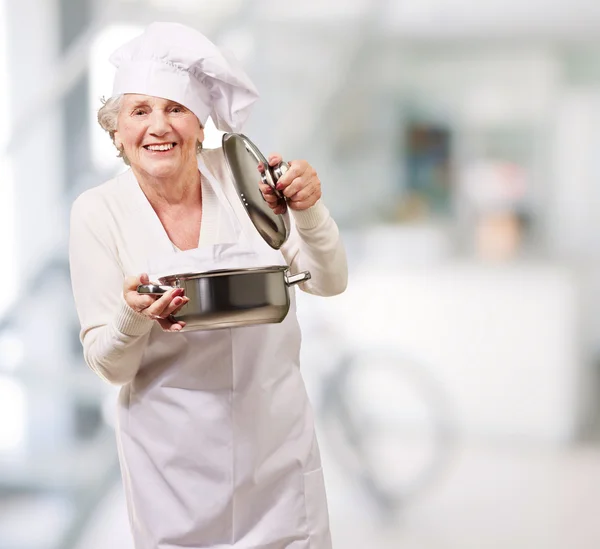 Portrait of cook senior woman opening sauce pan indoor — Stock Photo, Image
