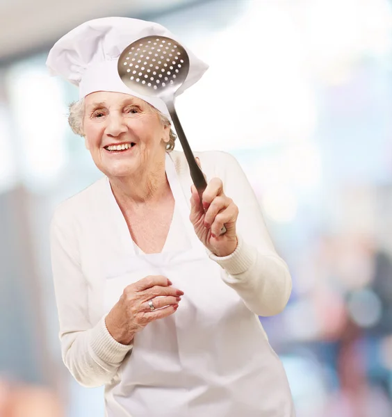 Portrait of sweet senior cook woman holding a metal spoon indoor — Stock Photo, Image