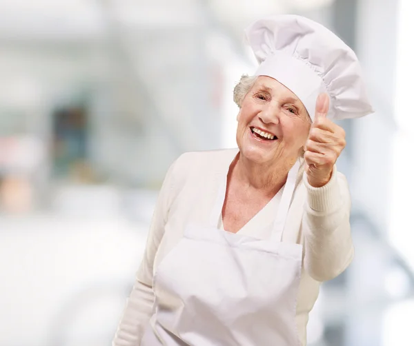 Retrato da cozinheira idosa fazendo bom gesto interior — Fotografia de Stock