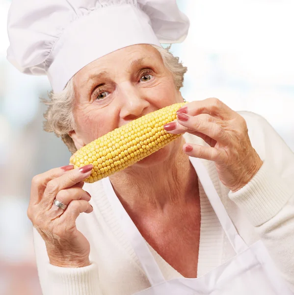 Portrait of cook senior woman eating corn cob indoor — Stock Photo, Image