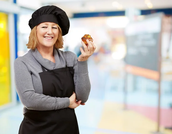 Portrait of middle aged cook woman holding a homemade muffin ind — Stock Photo, Image