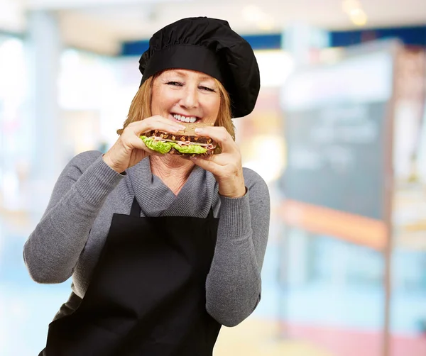 Mujer cocinera de mediana edad sosteniendo un sándwich vegetal interior — Foto de Stock