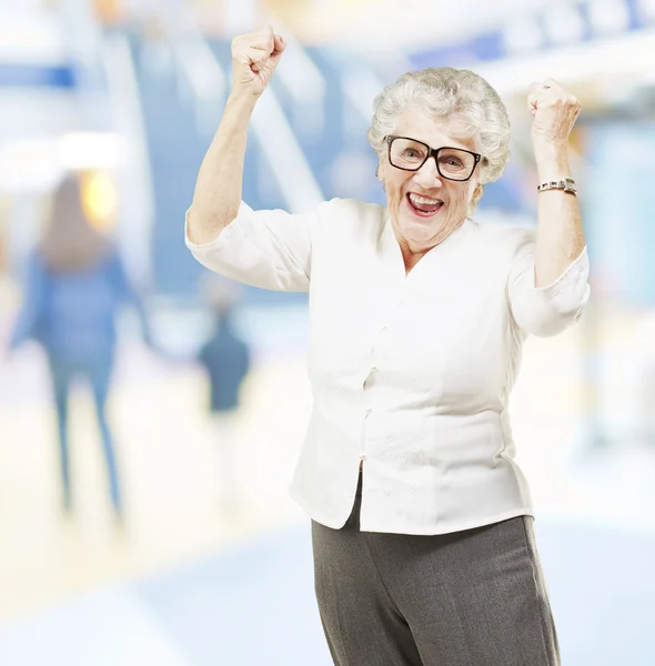 Портрет счастливой пожилой женщины, делающей победный жест в торговом центре — стоковое фото