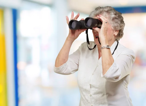 Porträt einer Seniorin, die durch ein Fernglas ins Haus blickt — Stockfoto