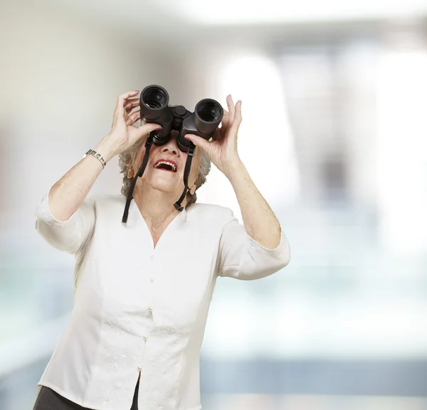 Portrét starší ženy dívá dalekohledem, vnitřní — Stock fotografie