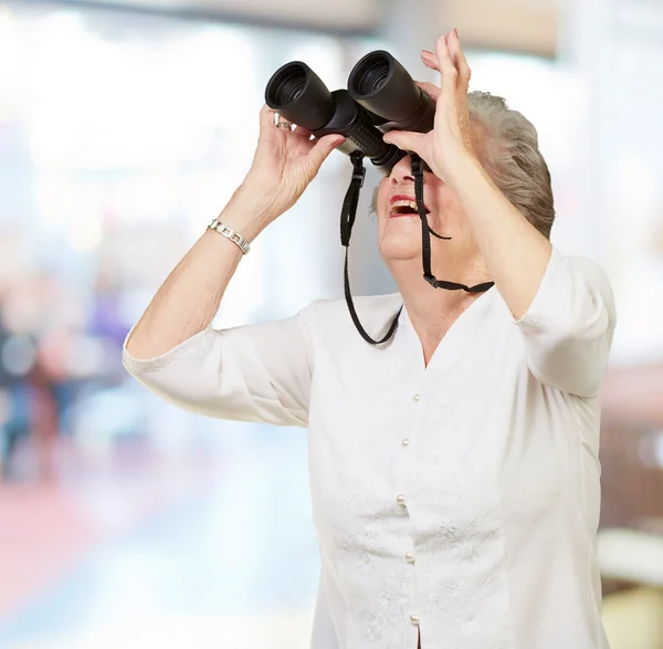 Porträtt av äldre kvinna som tittar genom en kikare inomhus — Stockfoto