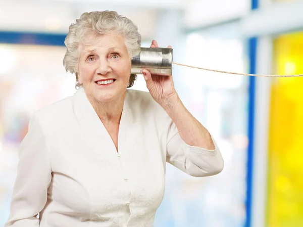 Retrato da mulher idosa ouvindo com lata de metal pode interior — Fotografia de Stock