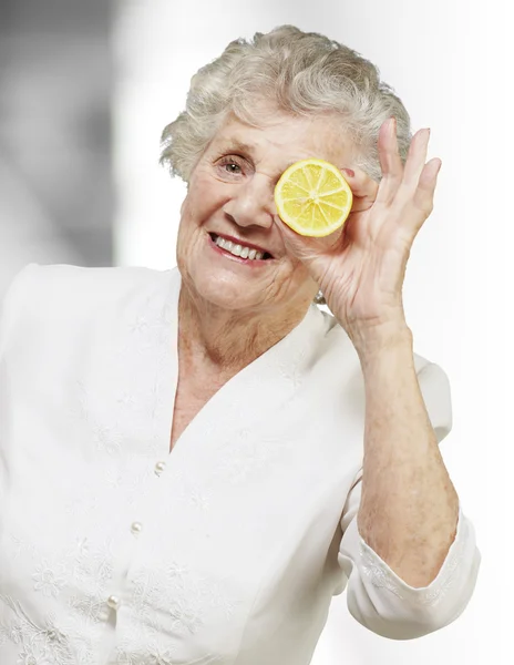 Portrait of senior woman with lemon in front of her eye, indoor — Stock Photo, Image