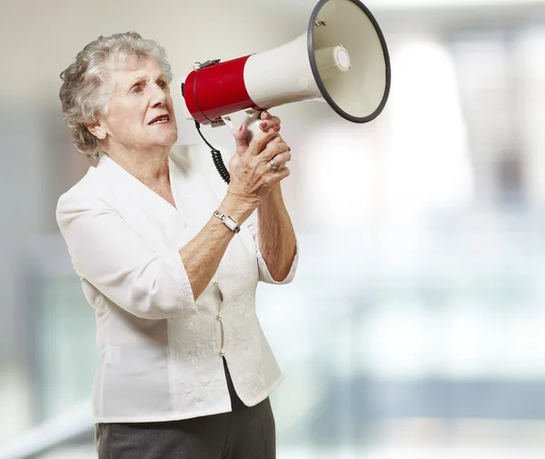Portrait of senior woman holding megaphone against a abstract ba — Stock Photo, Image