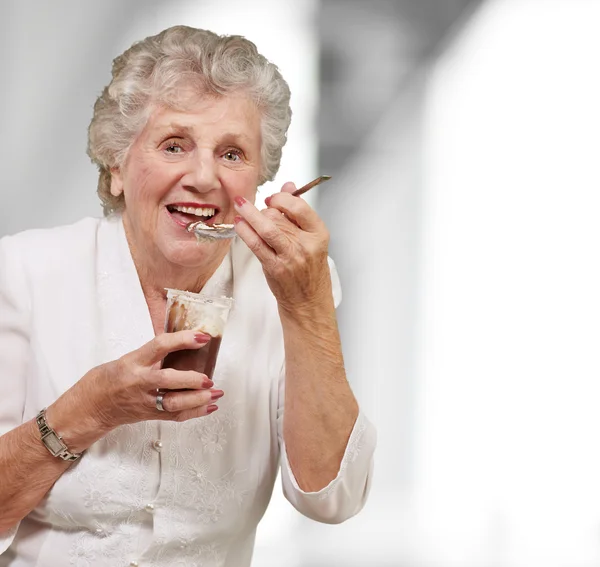 チョコレートとクリームカップを食べる先輩女性の肖像画室内 — ストック写真