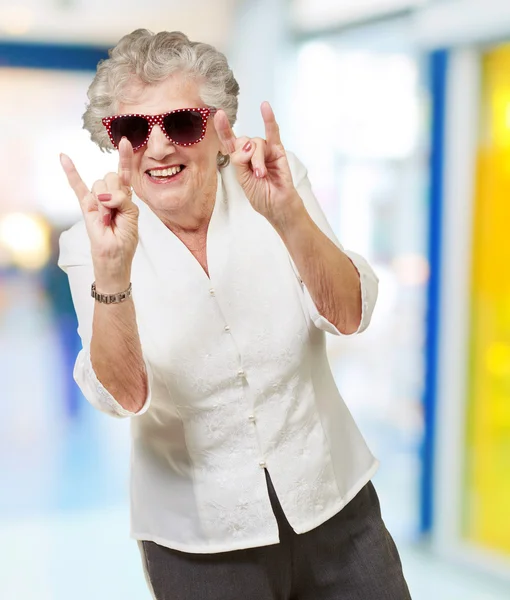 Retrato de una mujer mayor feliz haciendo símbolo de roca en el interior — Foto de Stock