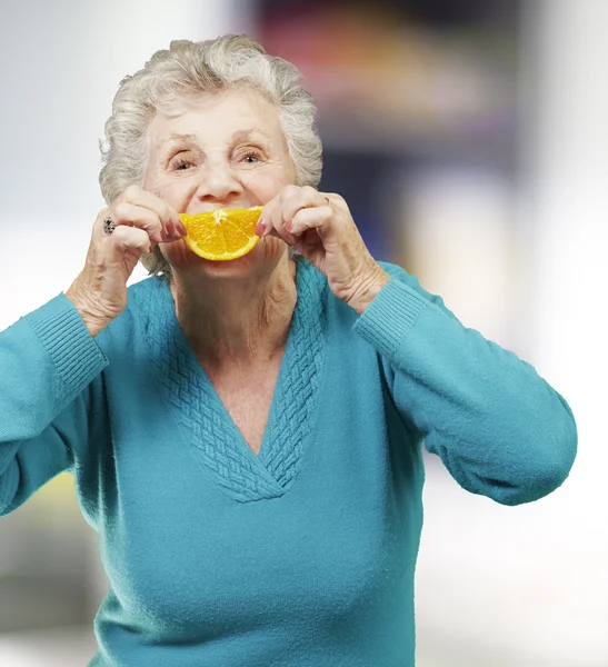 Portræt af senior kvinde holder en orange skive foran hende - Stock-foto