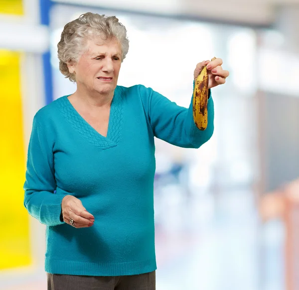Senior woman holding a rotten banana indoor — Stock Photo, Image