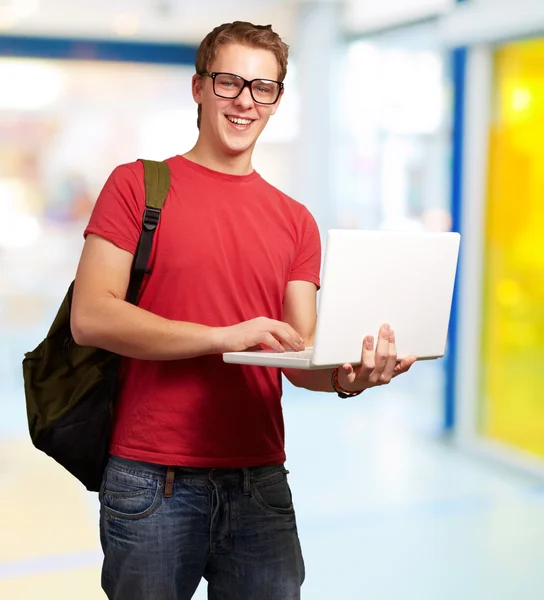Porträt eines jungen Mannes mit Laptop und Rucksack in der Hand — Stockfoto