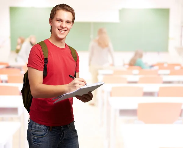 Porträt eines jungen Studenten, der im Klassenzimmer auf ein Notizbuch schreibt — Stockfoto