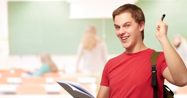 Retrato de estudiante guapo sosteniendo cuaderno y pluma en classro —  Fotos de Stock