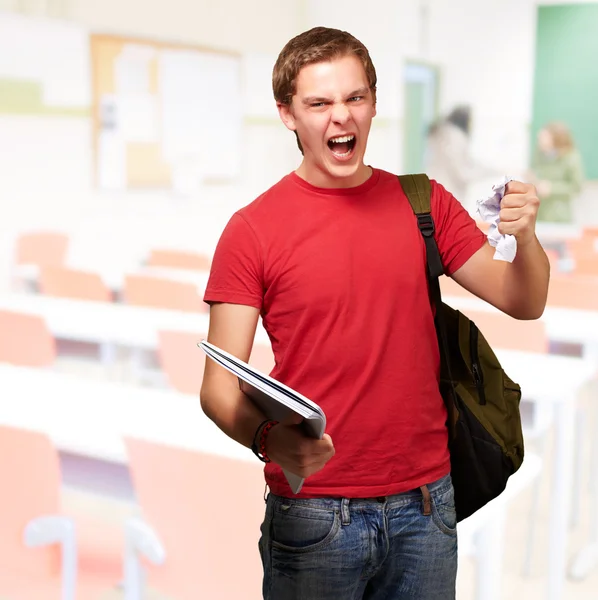 Mladý student rozzlobený muž hrubování list v učebně — Stock fotografie
