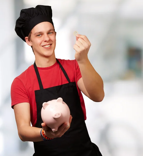 Retrato de jovem cozinheiro segurando moeda de euro e banco porquinho indo — Fotografia de Stock