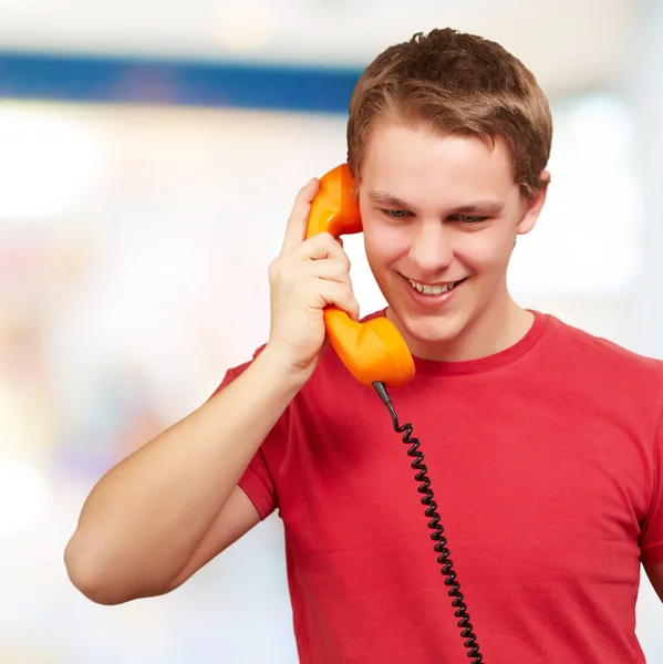 Porträt eines jungen Mannes, der auf einem Oldtimer-Telefon drinnen spricht — Stockfoto
