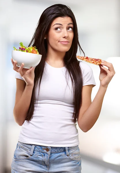 Ritratto di una giovane donna che sceglie pizza o insalata al coperto — Foto Stock