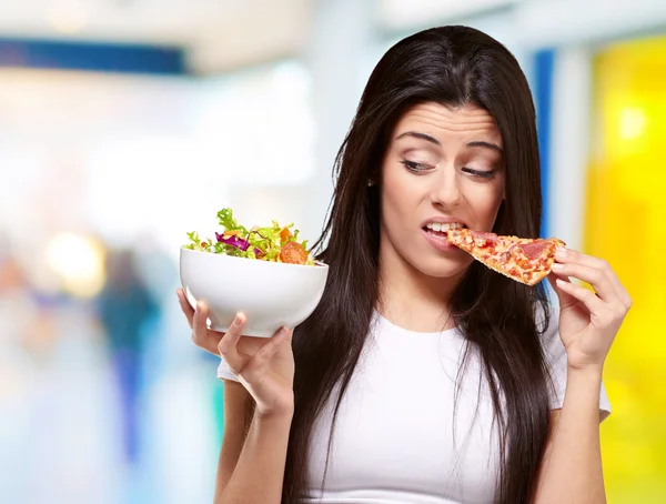 Porträtt av ung kvinna äta pizza och ser sallad inomhus — Stockfoto