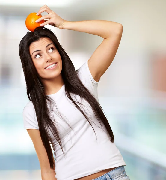 Retrato de mujer joven sosteniendo naranja en su cabeza interior —  Fotos de Stock