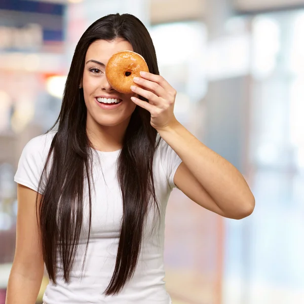 Портрет молодой женщины, смотрящей через крытый пончик — стоковое фото