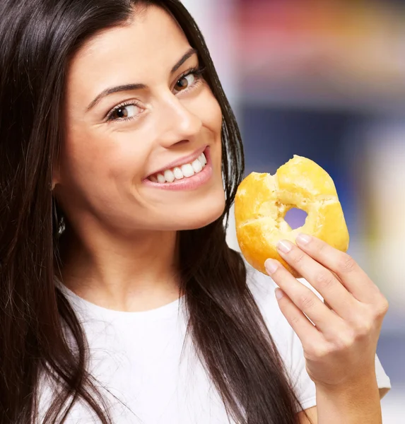 Portrait of young woman eating a donut against a abstract backgr — Stock Photo, Image