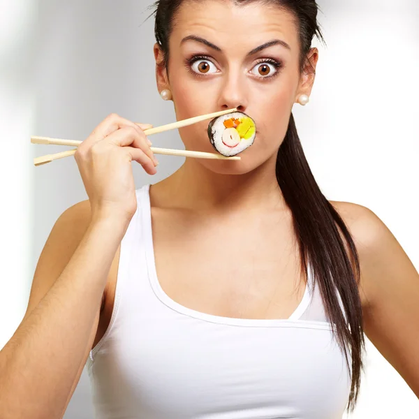 Ung kvinna som täcker hennes mun med en sushi pjäs, inomhus — Stockfoto