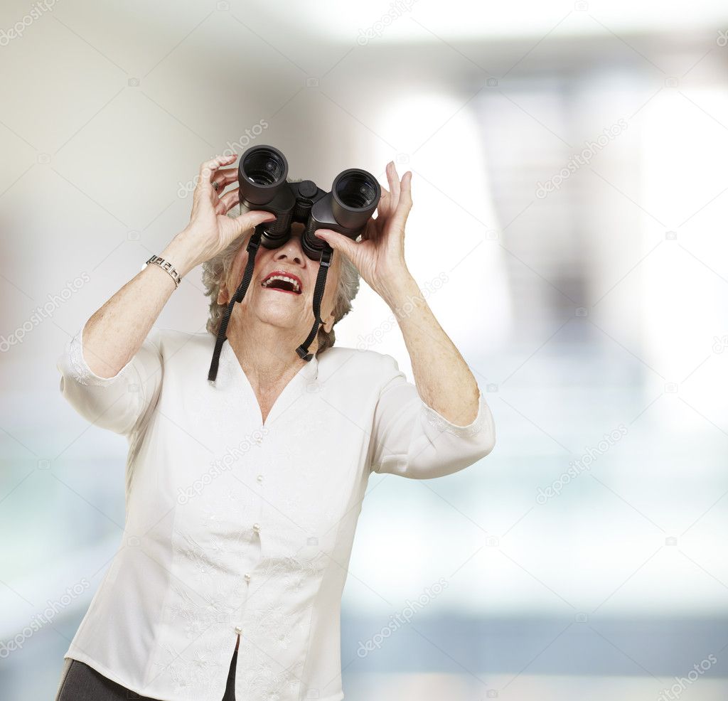 Portrait of senior woman looking through a binoculars, indoor