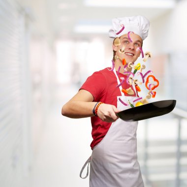 Portrait of young cook man cooking vegetables at modern building clipart