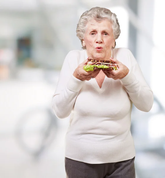 Retrato de mulher idosa segurando um delicioso sanduíche interior — Fotografia de Stock