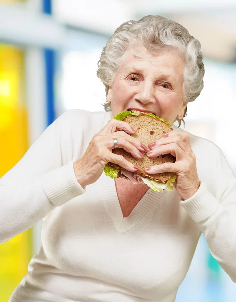 Portrett av en eldre kvinne som spiser vegetabilsk smørbrød innendørs – stockfoto