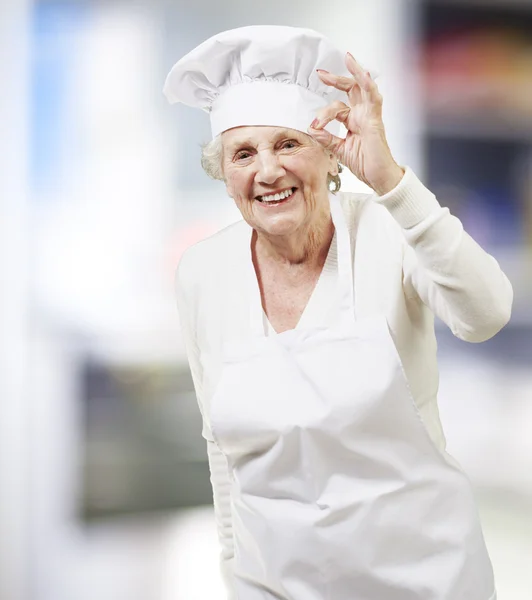 Mulher idosa cozinhar fazendo um excelente símbolo, interior — Fotografia de Stock