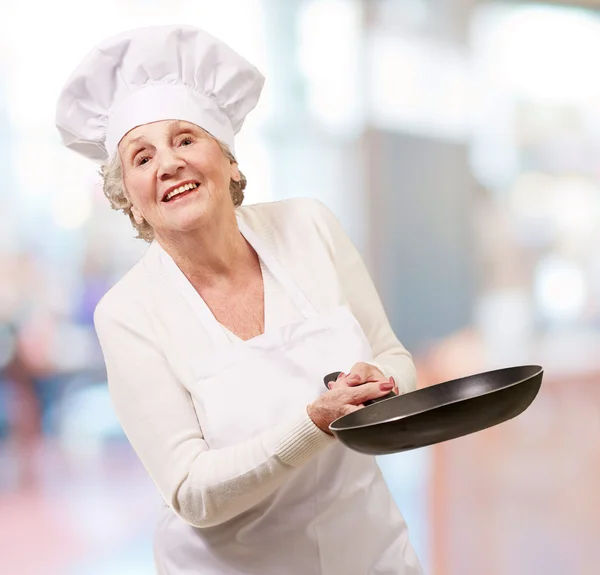 Portrét starší ženy přátelské kuchař drží pan vnitřní — Stock fotografie