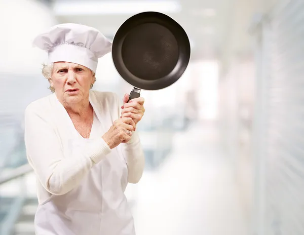 Köchin Seniorin wütend beim Versuch, mit Pfanne auf Hauseingang einzuschlagen — Stockfoto