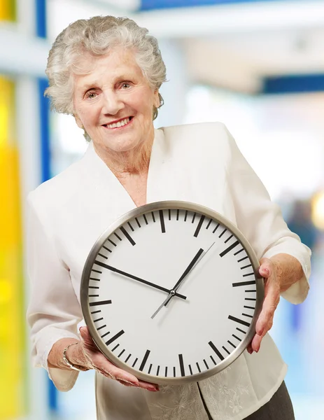 Portrait of a happy senior woman holding clock indoor — Stock Photo, Image