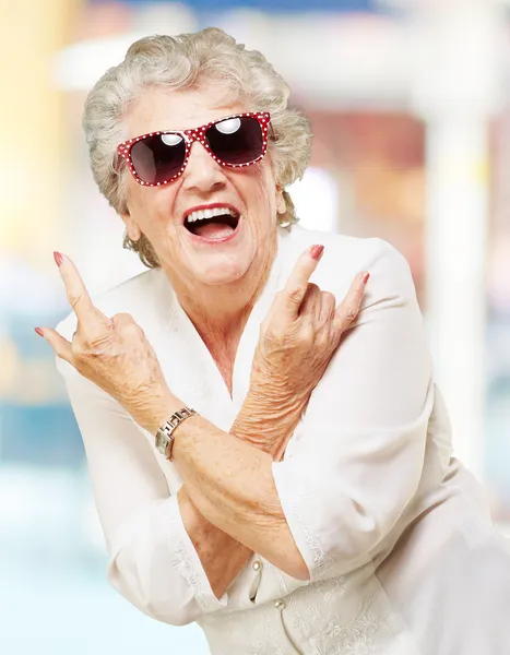 Portrait of senior woman smiling and wearing sunglasses against — Stock Photo, Image