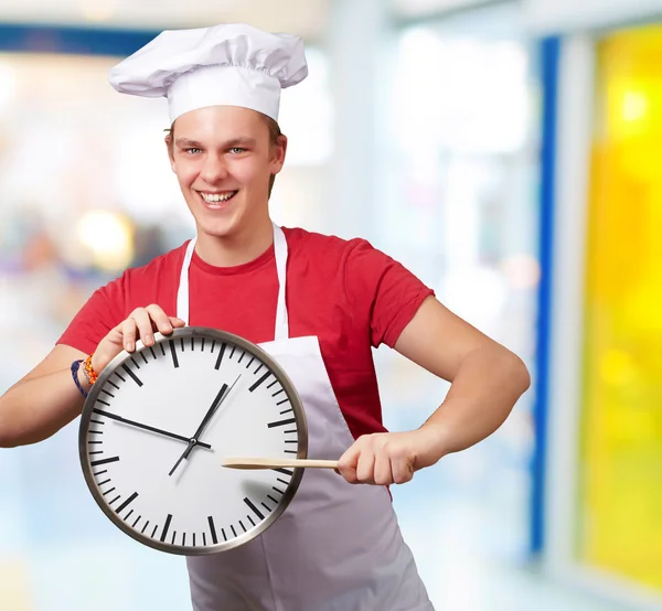 Retrato de jovem cozinheiro apontando um relógio interior — Fotografia de Stock