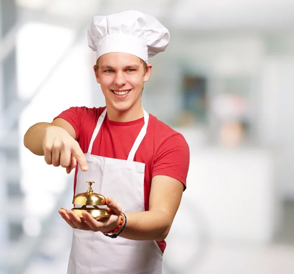 Portrait of young cook man pressing a golden bell indoor — Stock Photo, Image