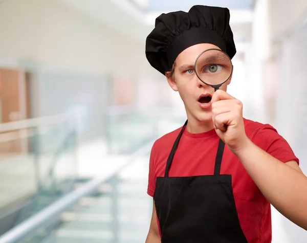 Retrato del joven cocinero mirando a través de una lupa en — Foto de Stock