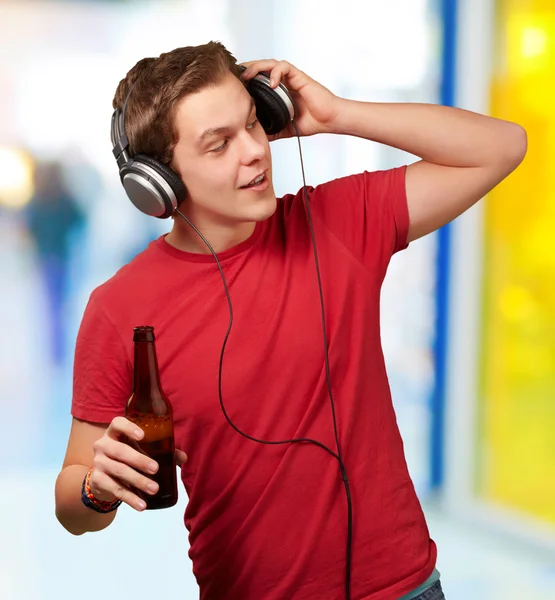Retrato de un joven escuchando música y sosteniendo cerveza en el interior — Foto de Stock