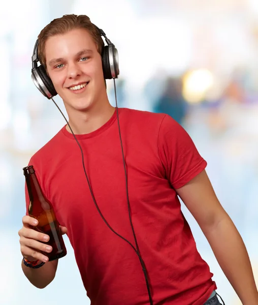 Porträt eines jungen Mannes, der Musik hört und drinnen Bier trinkt — Stockfoto