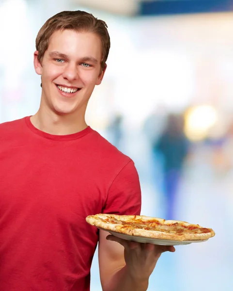 Молодой человек держит пиццу на абстрактном фоне — стоковое фото