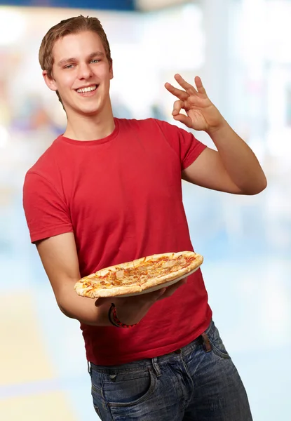 Pizza holding ve iyi bir jest indoo gidiyor genç adam portresi — Stok fotoğraf