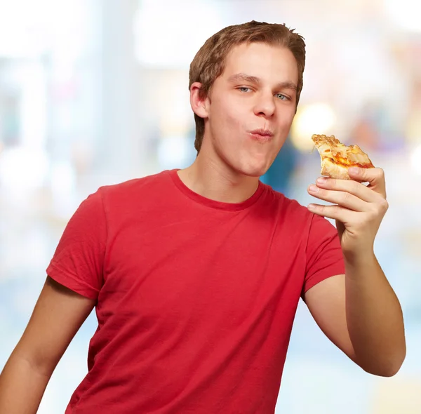 Portrait de jeune homme mangeant partie de pizza à l'intérieur — Photo