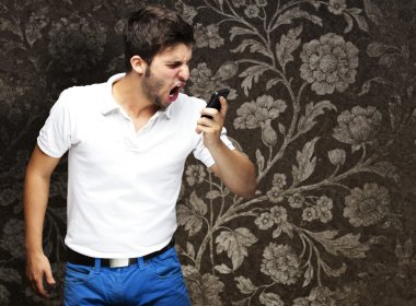 Portrait of angry young man shouting using mobile against a vint clipart