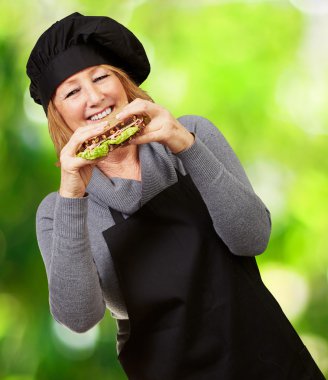 Middle aged cook woman holding a vegetal sandwich against a natu clipart