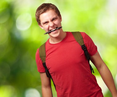 Portrait of angry young man biting pen against a nature backgrou clipart